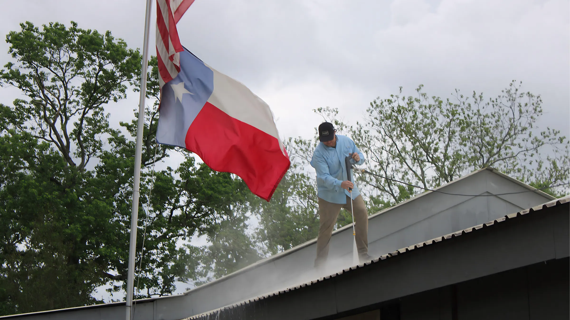 Kollin Goodman pressure washing a roof beside a Texas flag